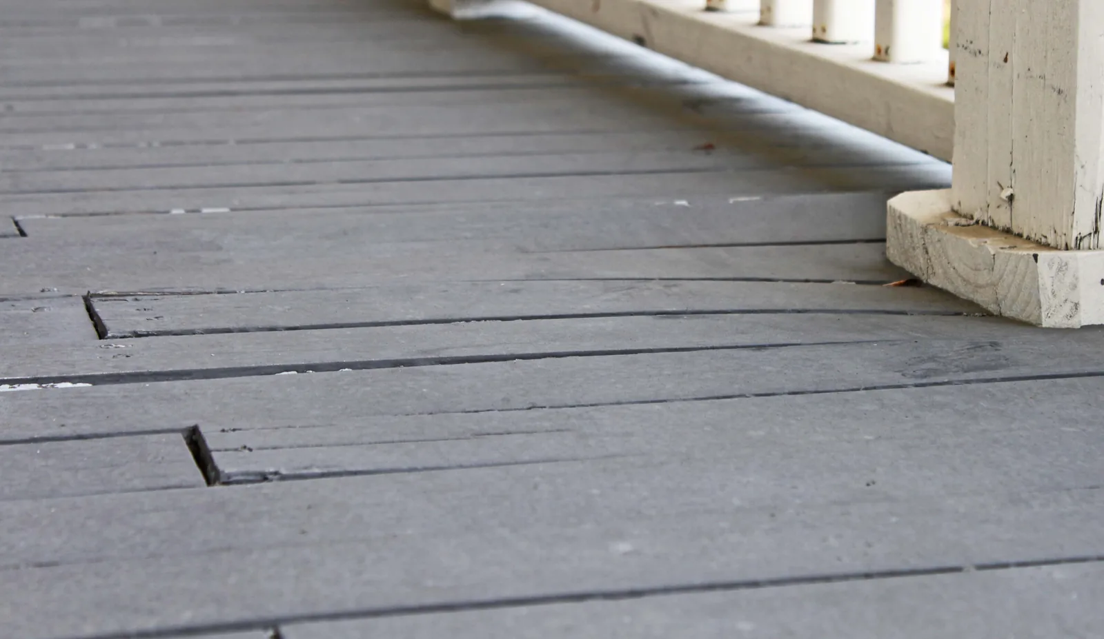 Gray deck boards lifting and separating beside a white railing post