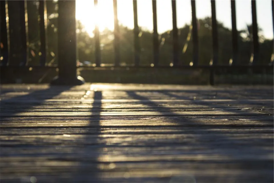 Low-angle view of deck boards at sunset with metal balusters casting long shadows