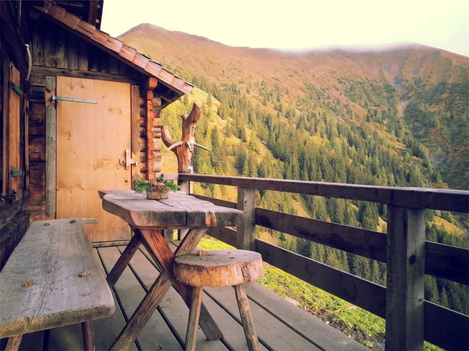 Rustic cabin deck with timber railing, plank table and log stools above a valley